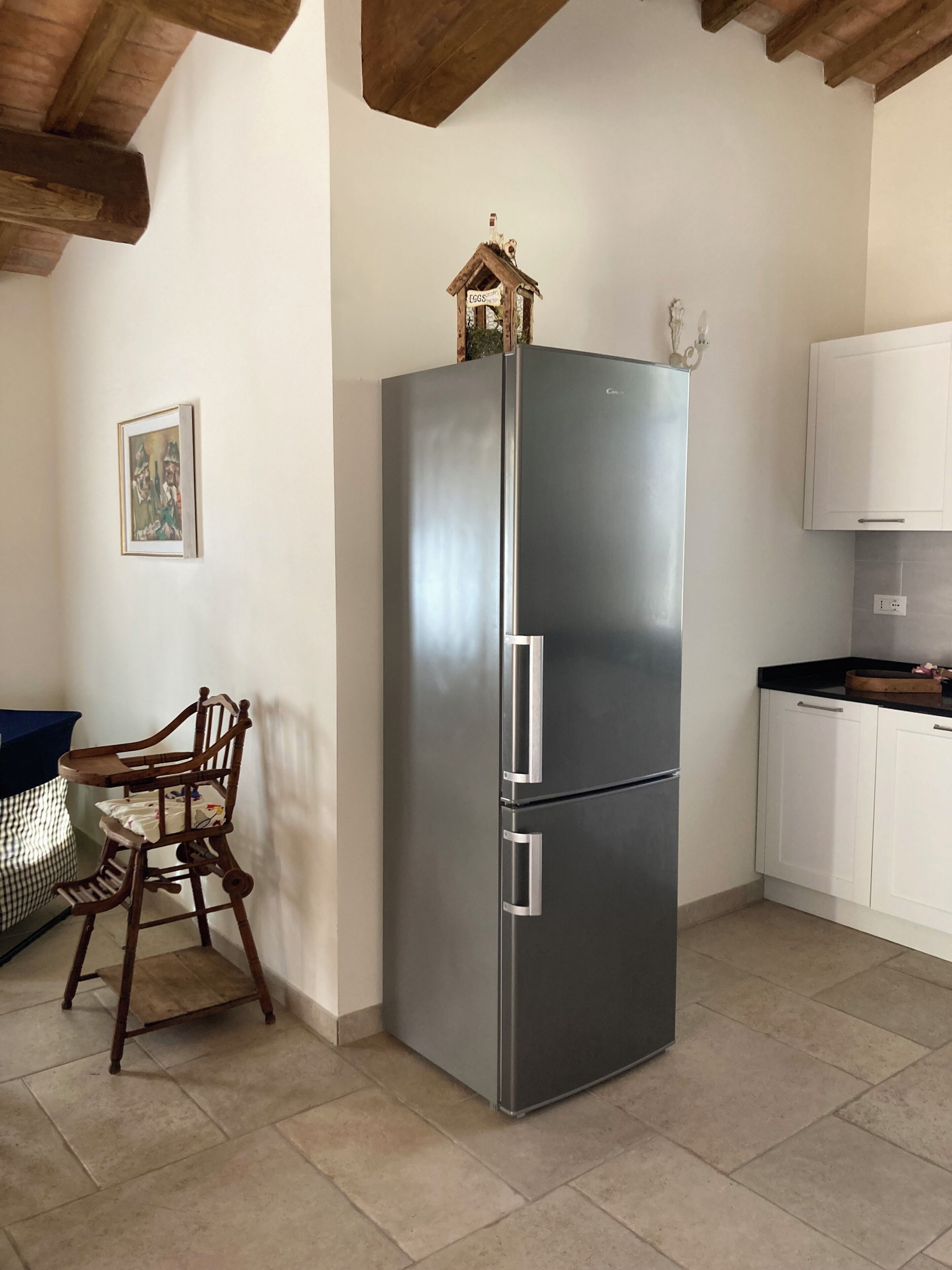 Eine Küche mit Edelstahl-Kühlschrank, Holzbalkendecke, einem Esstisch mit Stühlen und einem weißen Schrank.