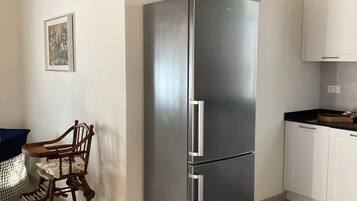 Eine Küche mit Edelstahl-Kühlschrank, Holzbalkendecke, einem Esstisch mit Stühlen und einem weißen Schrank.