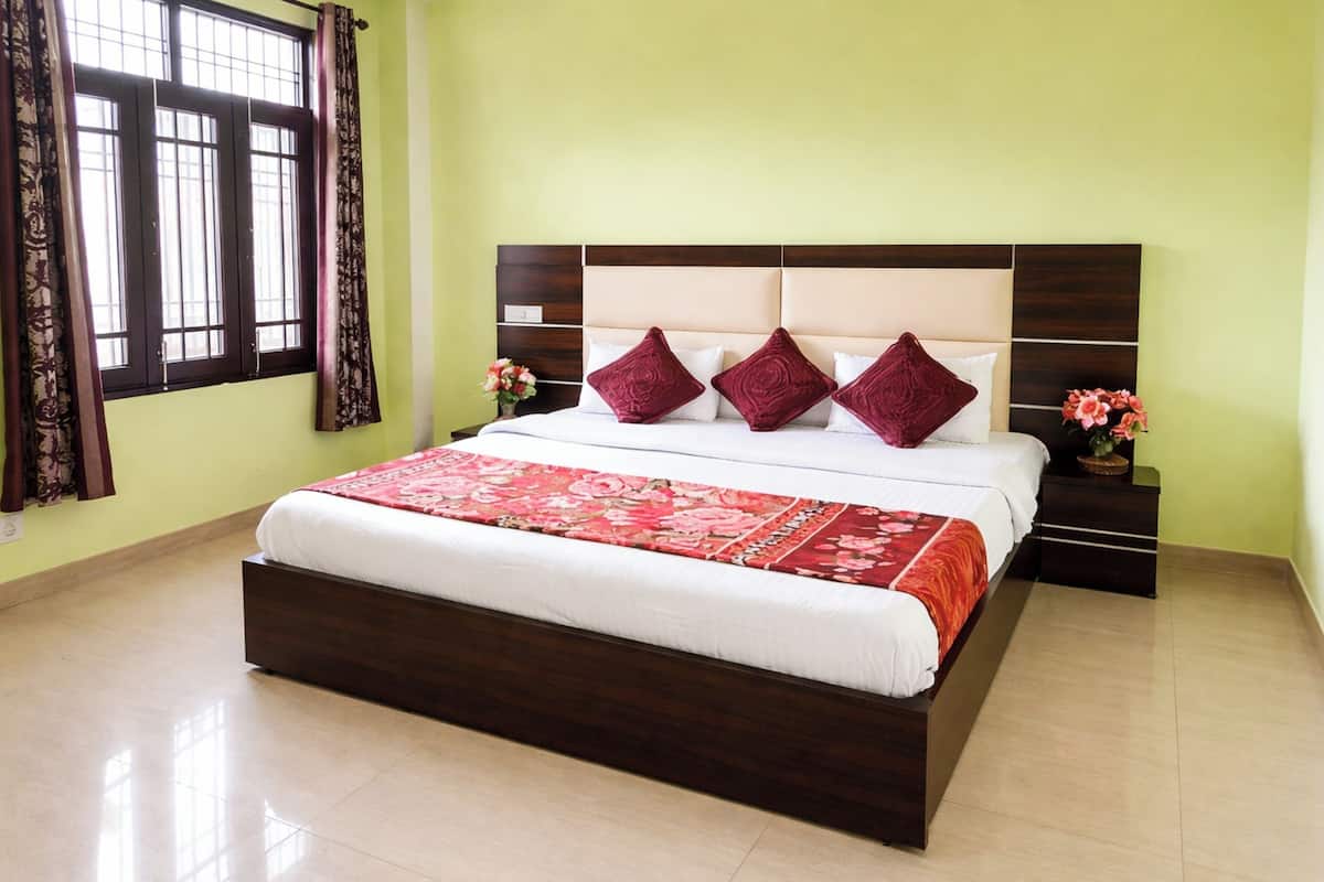 Una cama bien tendida con una colcha floral, un cabecero con detalles de madera y dos mesitas de noche con jarrones de flores.