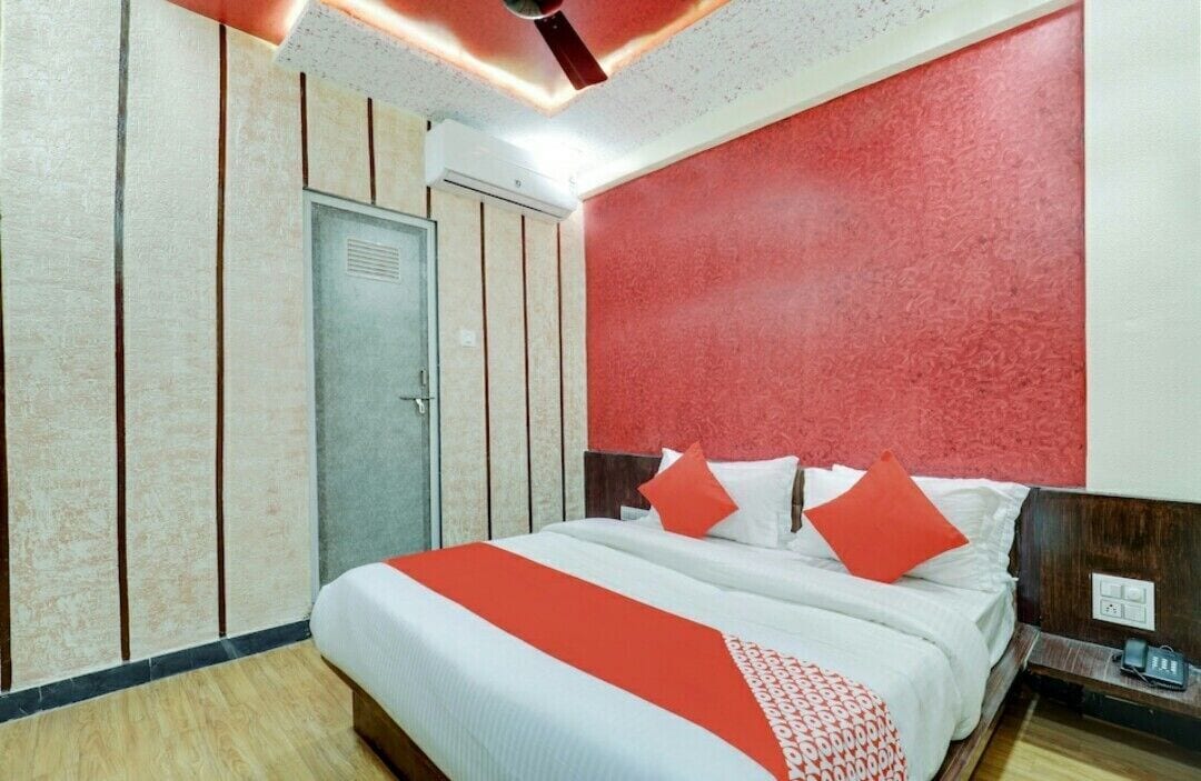 A hotel room with a large bed, a wooden headboard, a red accent wall, and a ceiling fan.