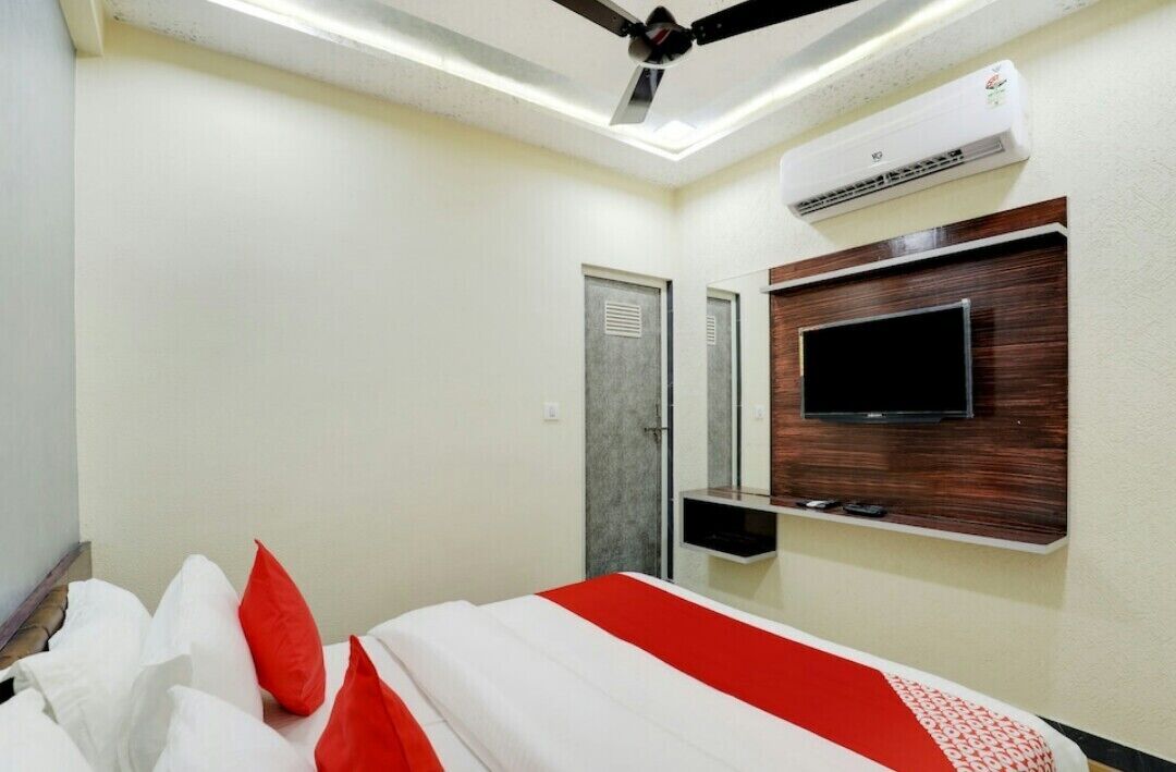 A hotel room with a bed, a ceiling fan, an air conditioning unit, a television mounted on the wall, and a door.