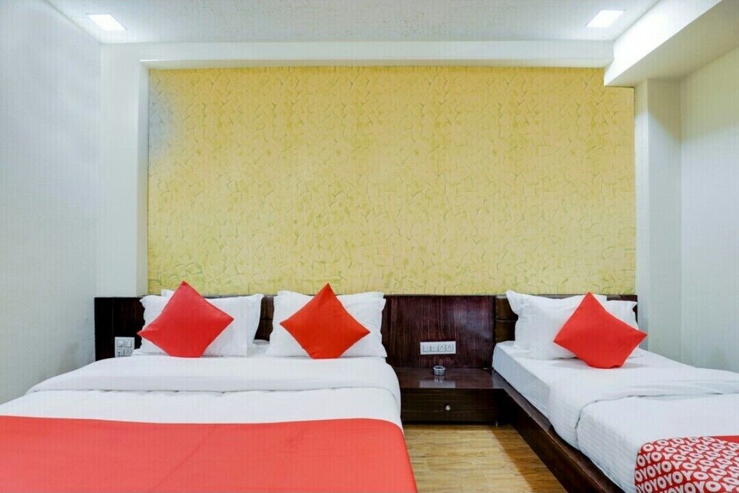 Habitación de hotel con dos camas, cabecero de madera, pared de textura amarilla y almohadas rojas.
