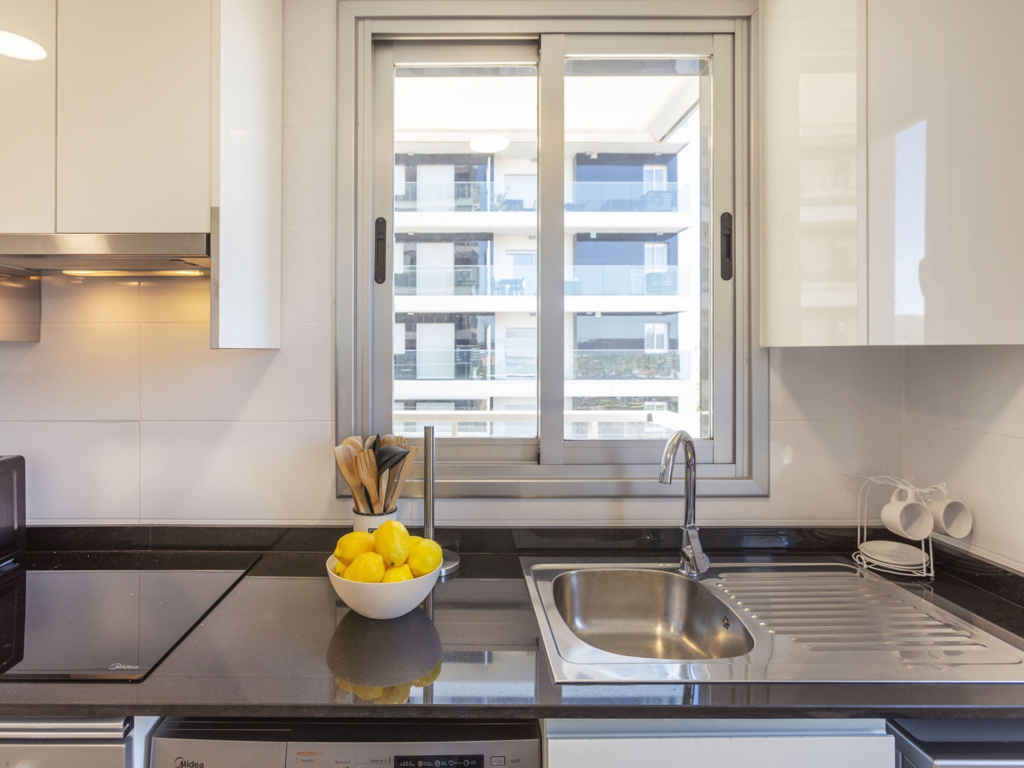 A modern kitchen with a built-in oven, a stainless steel sink, and a bowl of lemons on the counter.