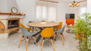 Un comedor con una mesa redonda, sillas, chimenea, ventilador de techo y televisión al fondo.
