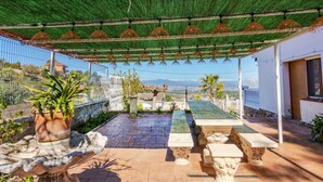 Un patio con un toldo verde, bancos de piedra, una fuente decorativa y vistas del paisaje.