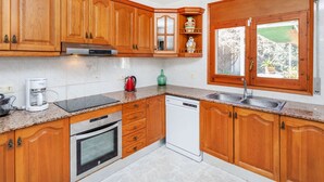 Una cocina con armarios de madera, lavavajillas, horno, cafetera y ventana con vista a un jardín.
