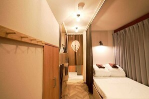 Une chambre d’hôtel de taille réduite, comprenant un lit, une armoire, un miroir et un petit coin salon.