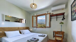 Una camera da letto con un letto, un comodino, una sedia, una finestra vista montagna e una lampada a sospensione.