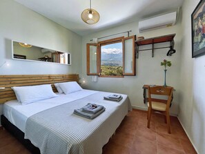 Ein Schlafzimmer mit Bett, Nachttisch, Stuhl, Fenster mit Bergblick und einer Pendelleuchte.