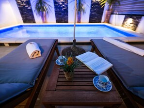 A poolside lounge area with two wooden loungers, a table with a book, a vase with flowers, and a pair of blue and white patterned cups. - Wohnung "Rustica mit exklusiver Nutzung des Pool by Interhome (Zadar)