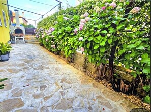 A cobblestone street with a row of green bushes and pink flowers, a yellow building, and a chimney. - Wohnung "Rustica mit exklusiver Nutzung des Pool by Interhome (Zadar)