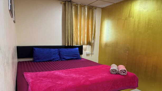 Una cama con un edredón rosa, dos almohadas azules y dos toallas enrolladas a un lado.