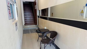 Un pasillo con una escalera, un letrero de 'No Fumar', un aviso y una pequeña mesa con dos sillas de mimbre.