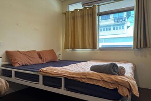 A single bed with a blue mattress, brown pillows, and a rolled-up blanket. - The House Hostel (Bangkok)