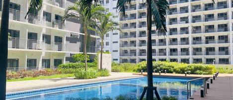 A swimming pool surrounded by greenery and a multi-story building with balconies.