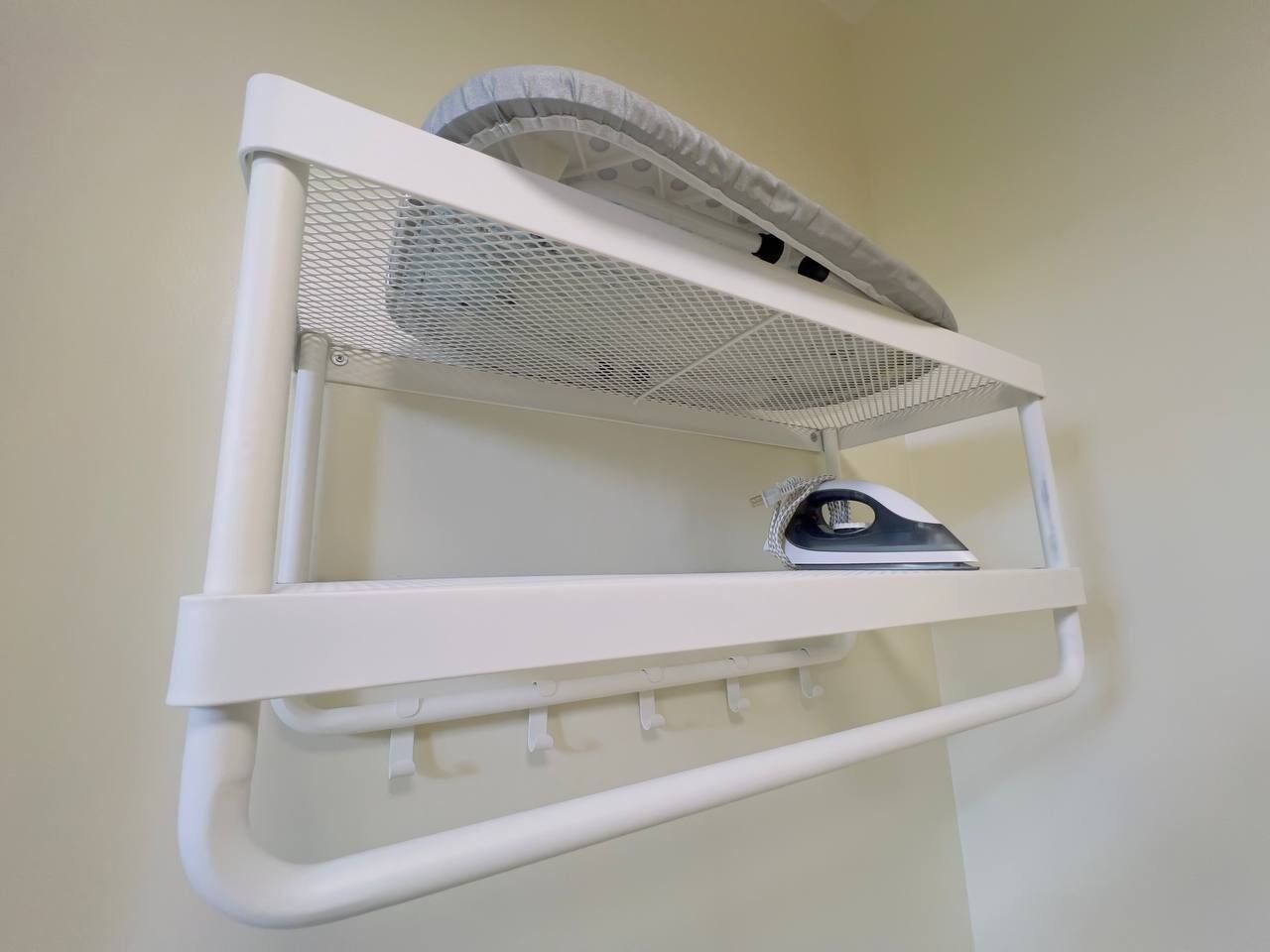 A white wall-mounted shelf with a mesh laundry basket and an iron.