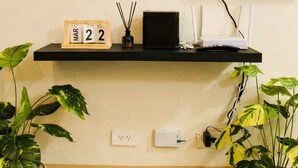 Un téléviseur à écran plat fixé au mur, avec une étagère en dessous sur laquelle sont posés un calendrier, un petit haut-parleur et une plante.