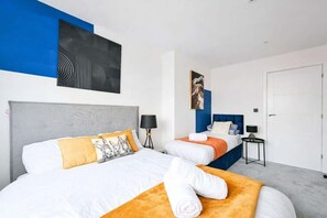 A hotel room with two beds, a grey headboard, a blue accent wall, and a white door. - Sleeps 6 | Hendon | Parking + Fast WiFi (London)