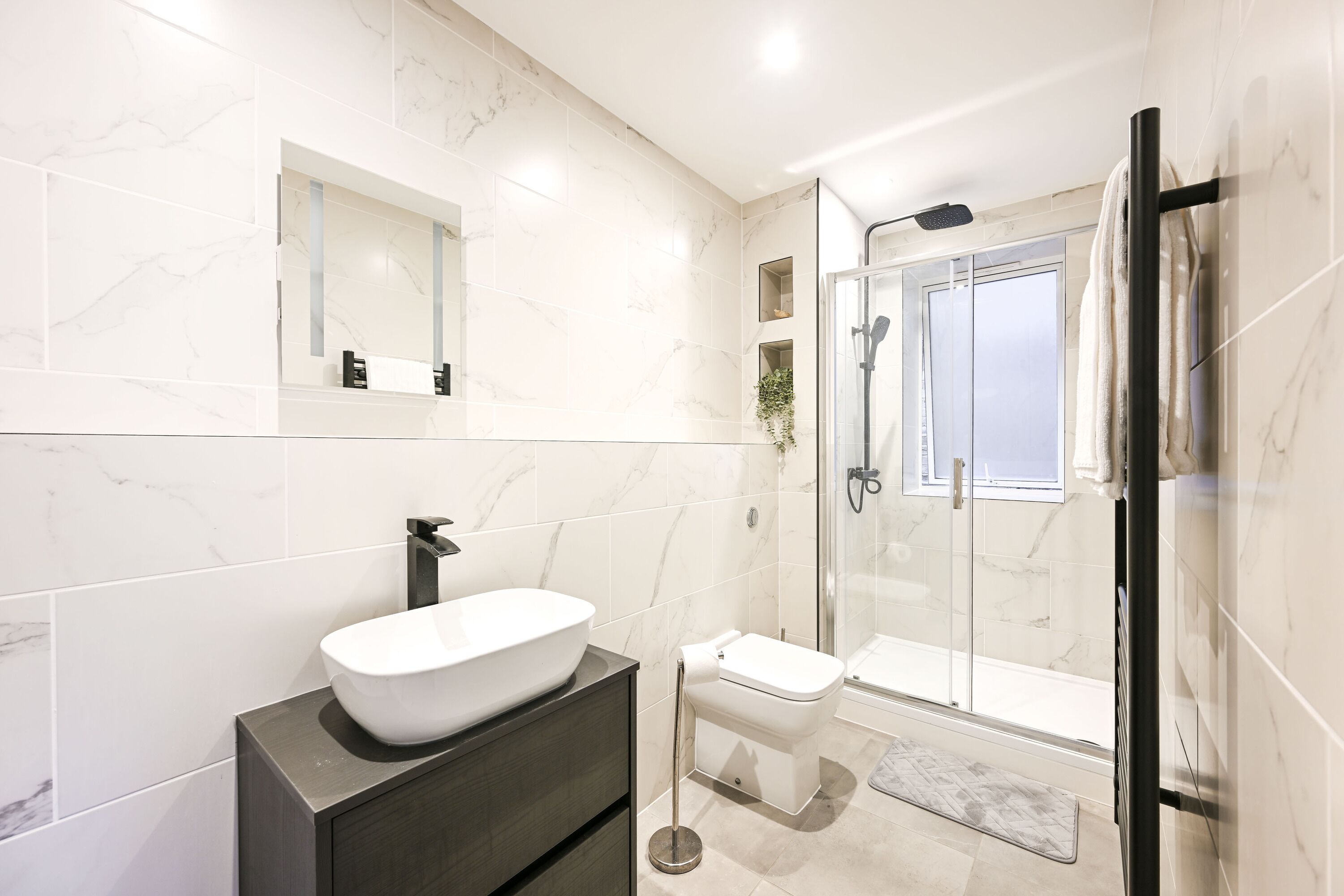 A modern bathroom with a large mirror, a vessel sink, a toilet, and a glass-enclosed shower.