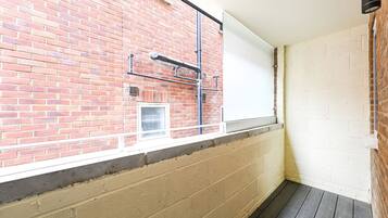 A room with a brick wall, a window with a white blind, and a wooden floor.
