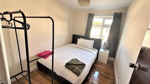 Un dormitorio con una cama, una mesita de noche, una ventana con cortinas y una lámpara colgante.