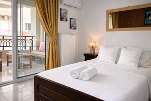 A hotel room with a bed, a nightstand, a lamp, a window with curtains, and a view of the outside balcony. - BH1041 - A - Summer Home (Agios Nikolaos)