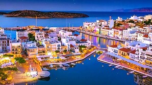 A coastal town with buildings along the waterfront, a marina, and a small island in the background. - BH1041 - A - Summer Home (Agios Nikolaos)