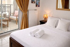 A hotel room with a bed, two pillows, a nightstand with a lamp, a window with curtains, a chair, and a radiator. - BH1041 - A - Summer Home (Agios Nikolaos)