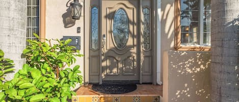 Une entrée d’immeuble avec le numéro « 138 » au-dessus de la porte, un paillasson et un petit arbre au premier plan.