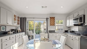 Una cocina moderna con armarios blancos, una mesa de comedor de vidrio y vistas al exterior.