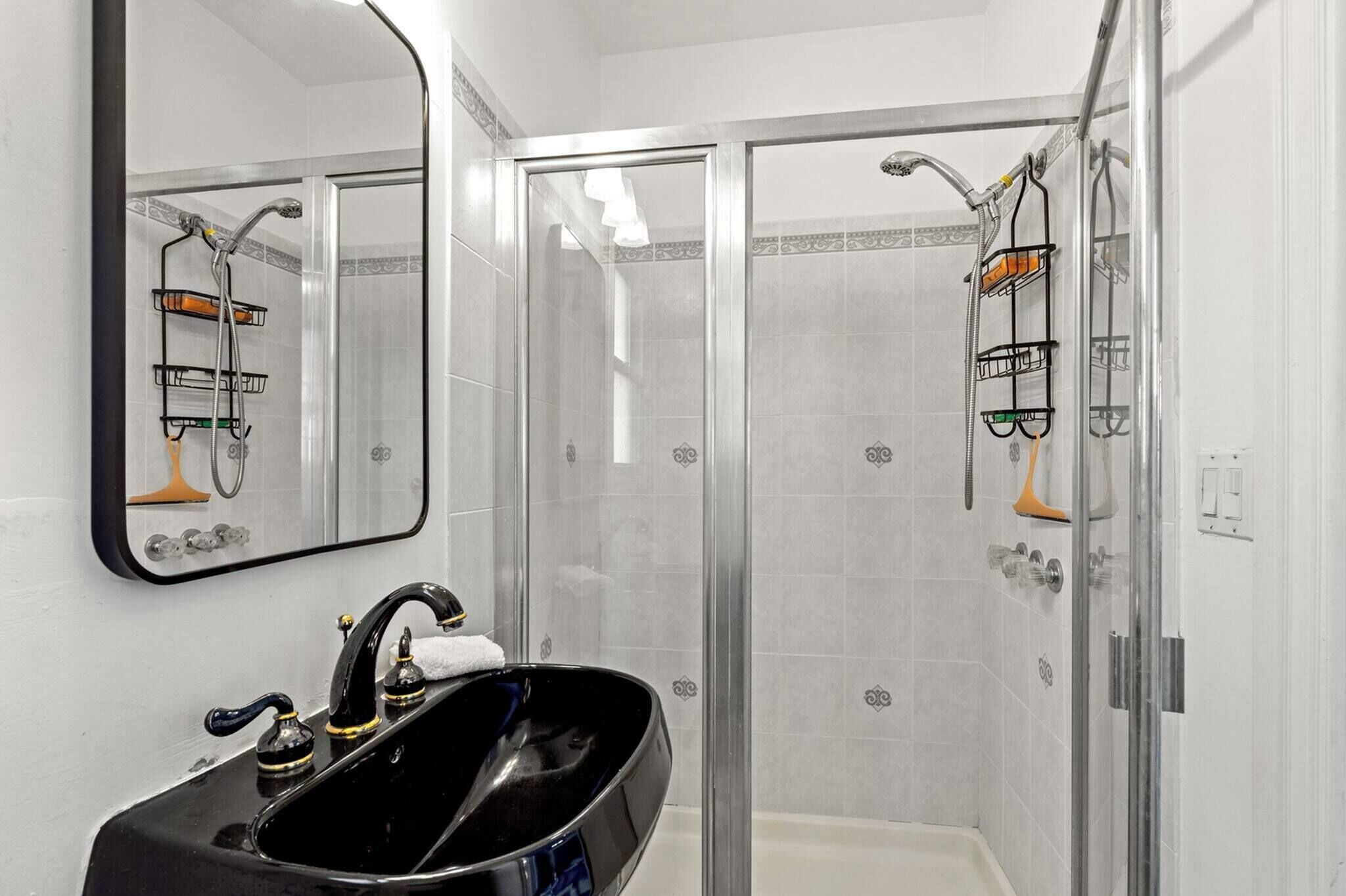 A bathroom with a black sink, a mirror, a shower with glass doors, and tiled walls.
