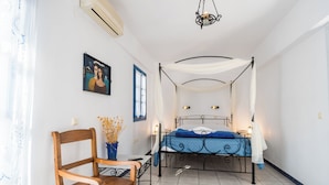 Quarto com uma cama de dossel, uma cadeira de madeira, uma mesinha e ar-condicionado fixado na parede.