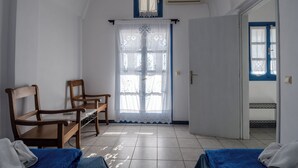 Quarto com duas cadeiras de madeira, cama com manta azul, porta branca e janela com moldura azul.
