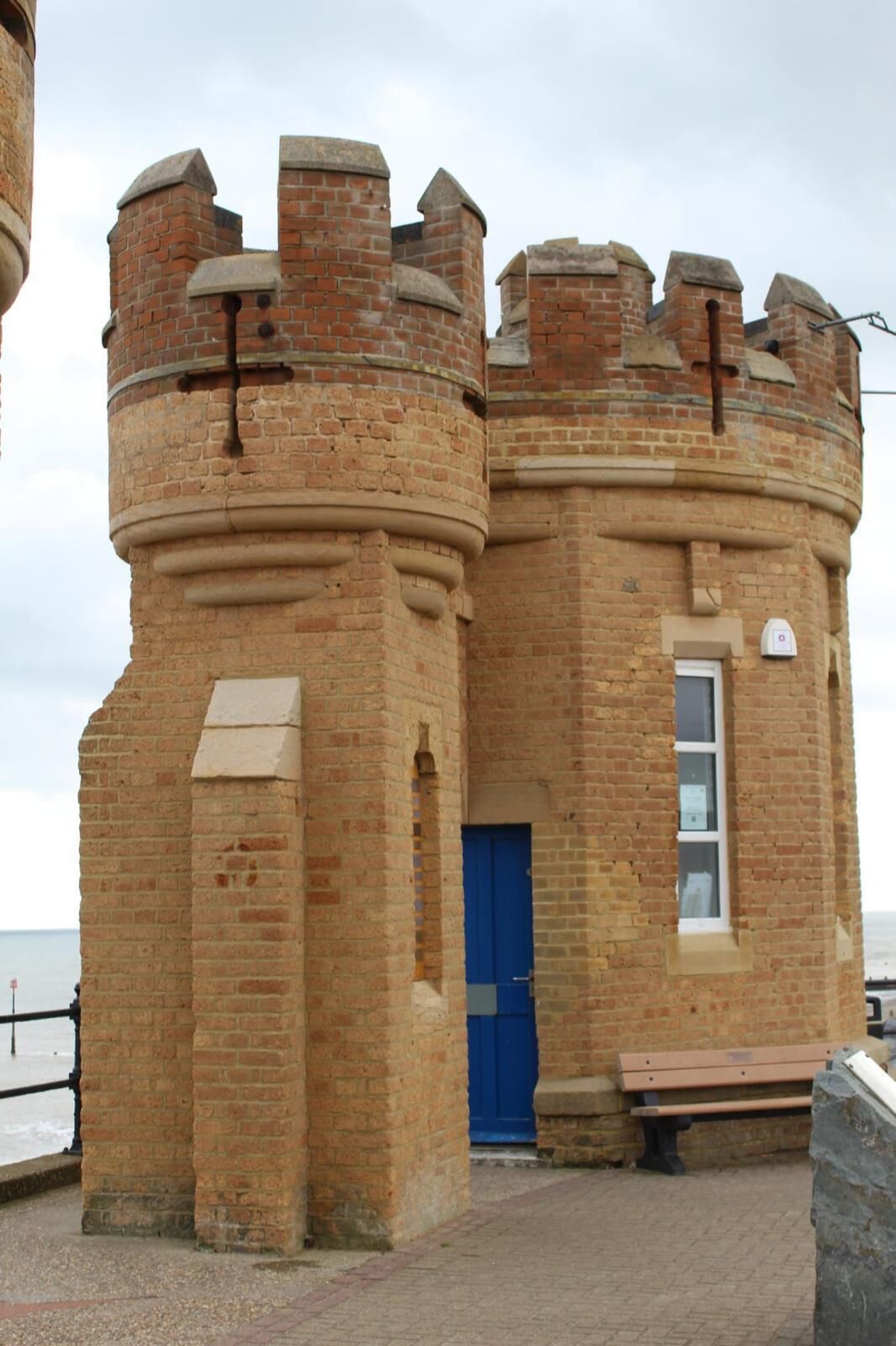 A brick tower with a blue door, a bench, and a stone wall.
