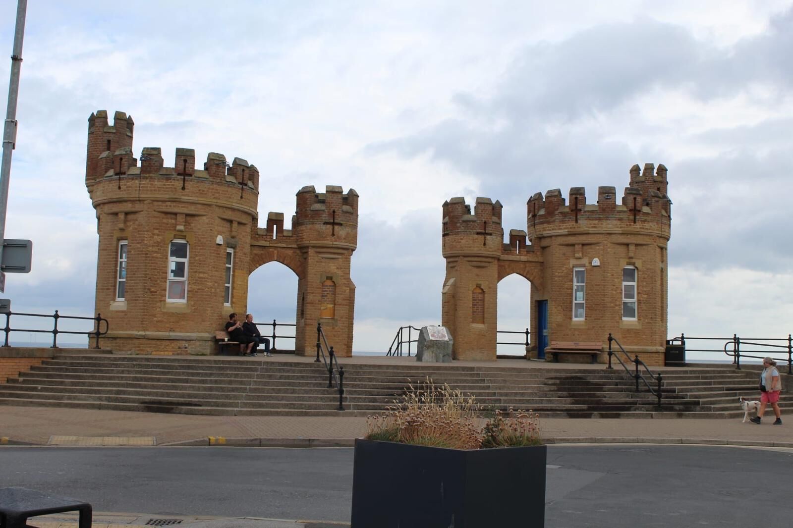 A historic brick structure with two towers and arched gateways, featuring steps leading up to it.