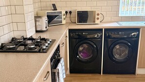 A modern kitchen with a gas stove, microwave, and two washing machines. - Spacious House Sleeps 10 -Near BikePark Wales -Central -Parking (Troedyrhiw)