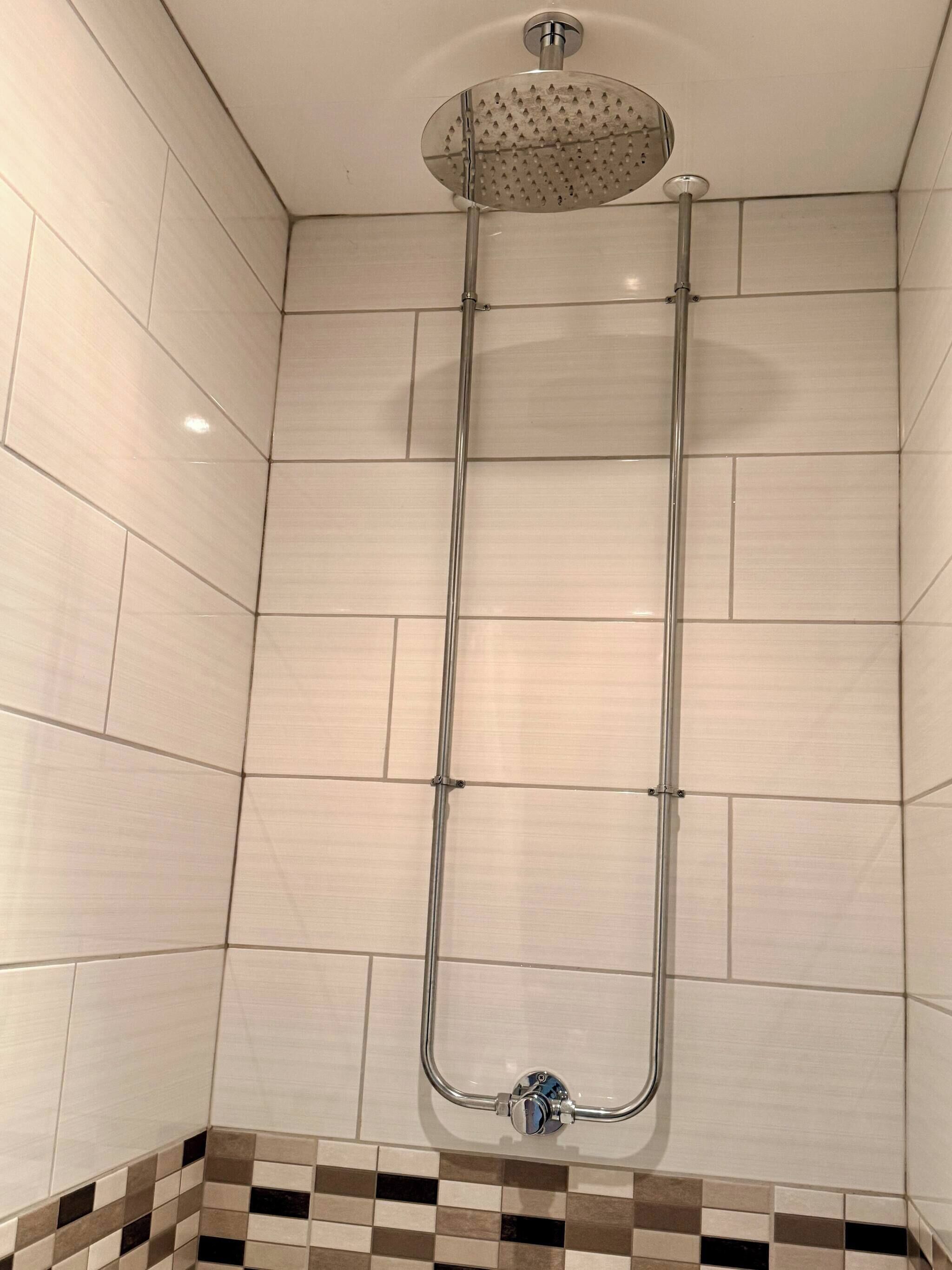 Eine Dusche mit Handbrause, einer vertikalen Metallstange und einem gefliesten Boden mit Schachbrettmuster.