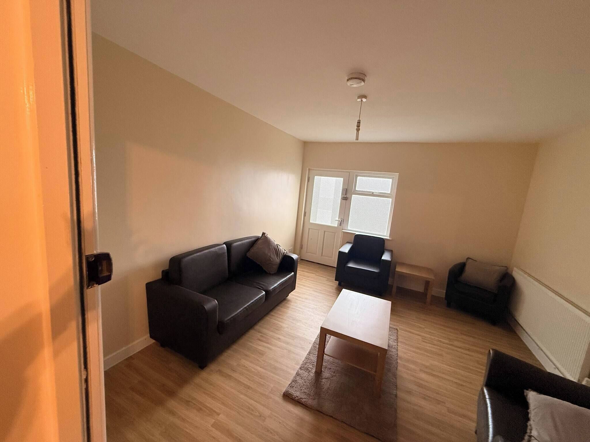 A living room with a sofa, a coffee table, and a chair. There is a door leading to another room.