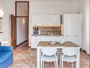 Une cuisine moderne avec des meubles blancs, un plan de travail en bois, un four à micro-ondes, une bouilloire et une table à manger avec deux chaises.