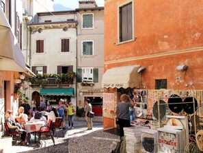 Une rue étroite avec des tables en terrasse, un stand de café et une boutique proposant des articles aux couleurs vives.