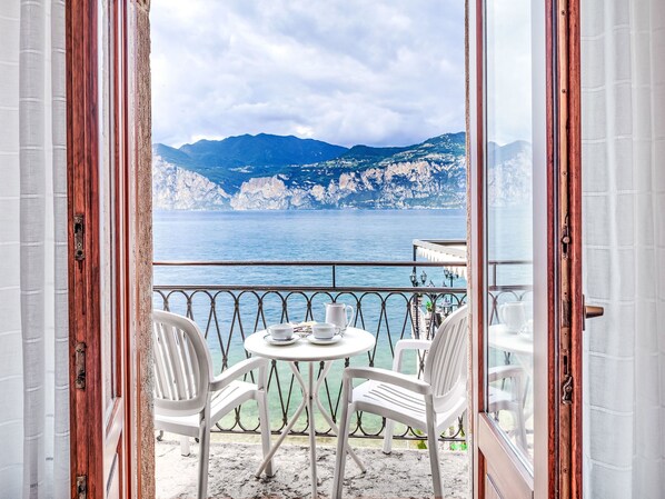 Un balcon ouvert, avec une table et des chaises, offrant une vue sur la côte et les montagnes.