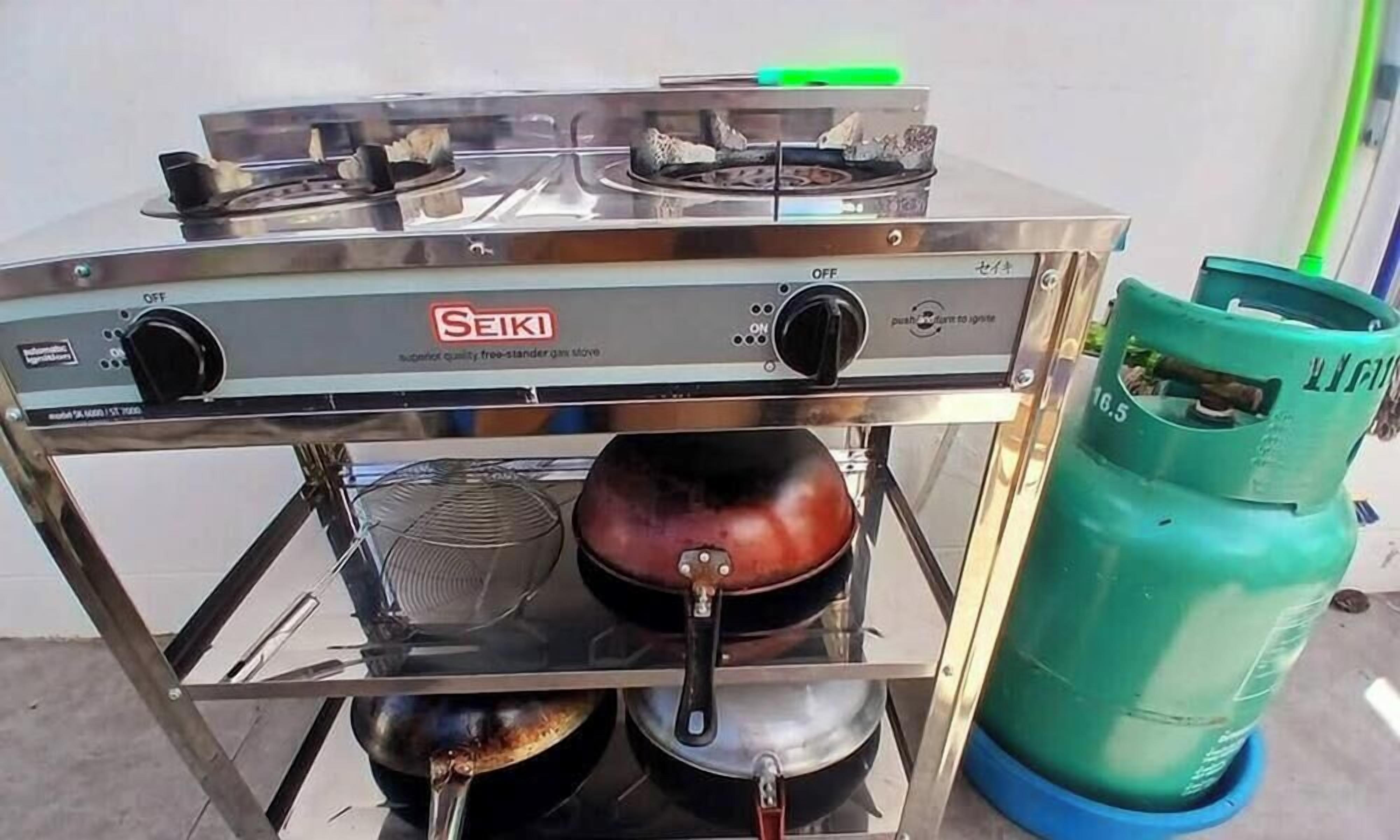 Una cocina con estufa a gas, ollas y un cilindro de gas.