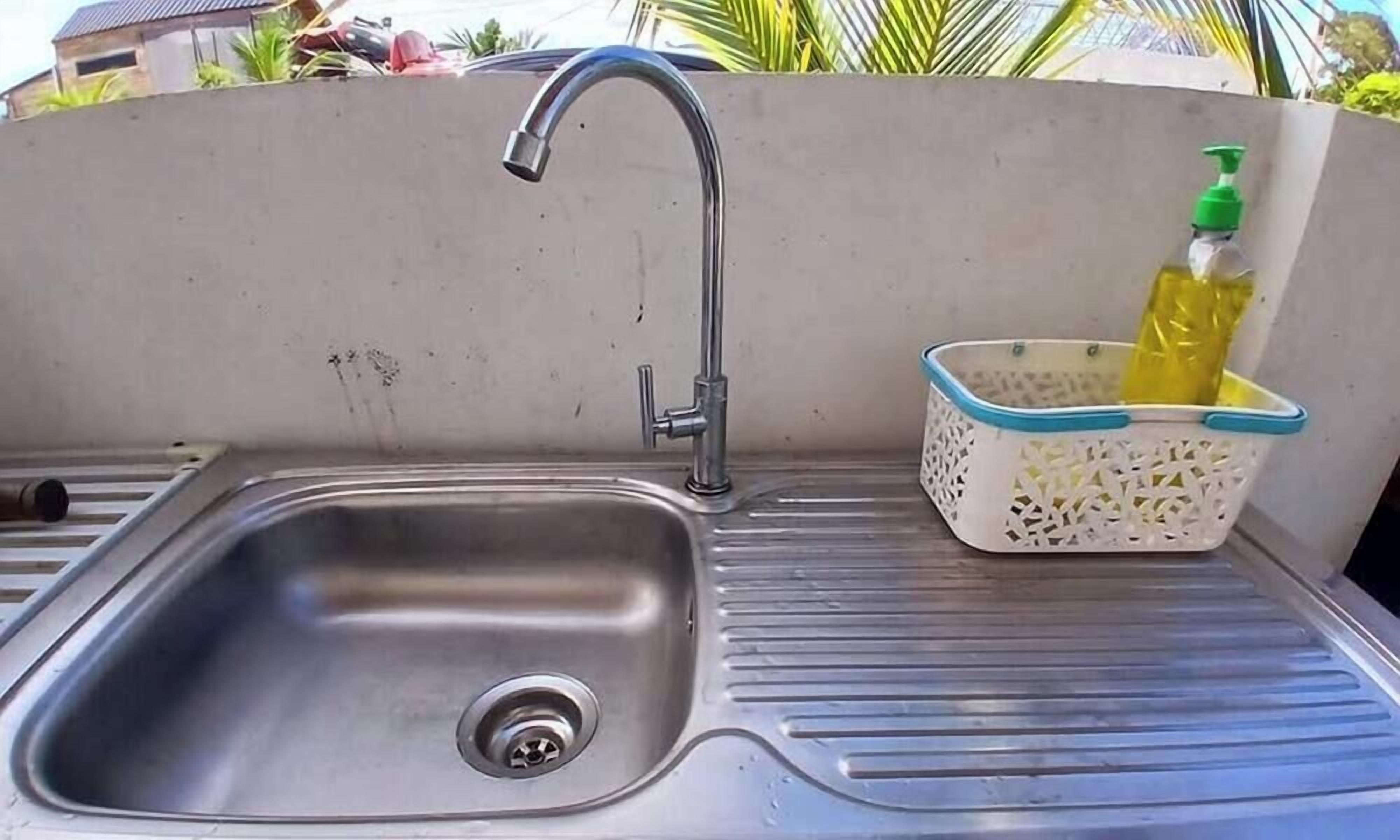 A stainless steel sink with a single faucet, a drainage hole, and a white basket with a blue rim containing a yellow bottle.