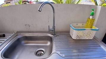 A stainless steel sink with a single faucet, a drainage hole, and a white basket with a blue rim containing a yellow bottle.