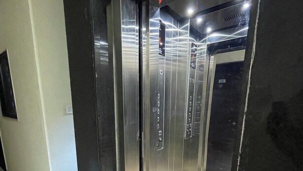 Een lift met een metalen afwerking, een bedieningspaneel met knoppen en een verdiepingaanduiding.