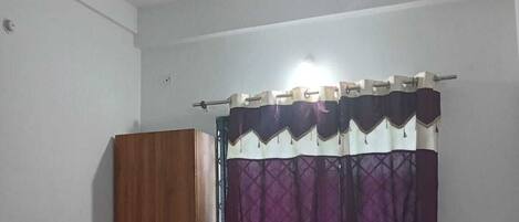 Ein Schlafzimmer mit einem Bett, einem Deckenventilator, einem Kleiderschrank und einem Fenster mit violetten Vorhängen.