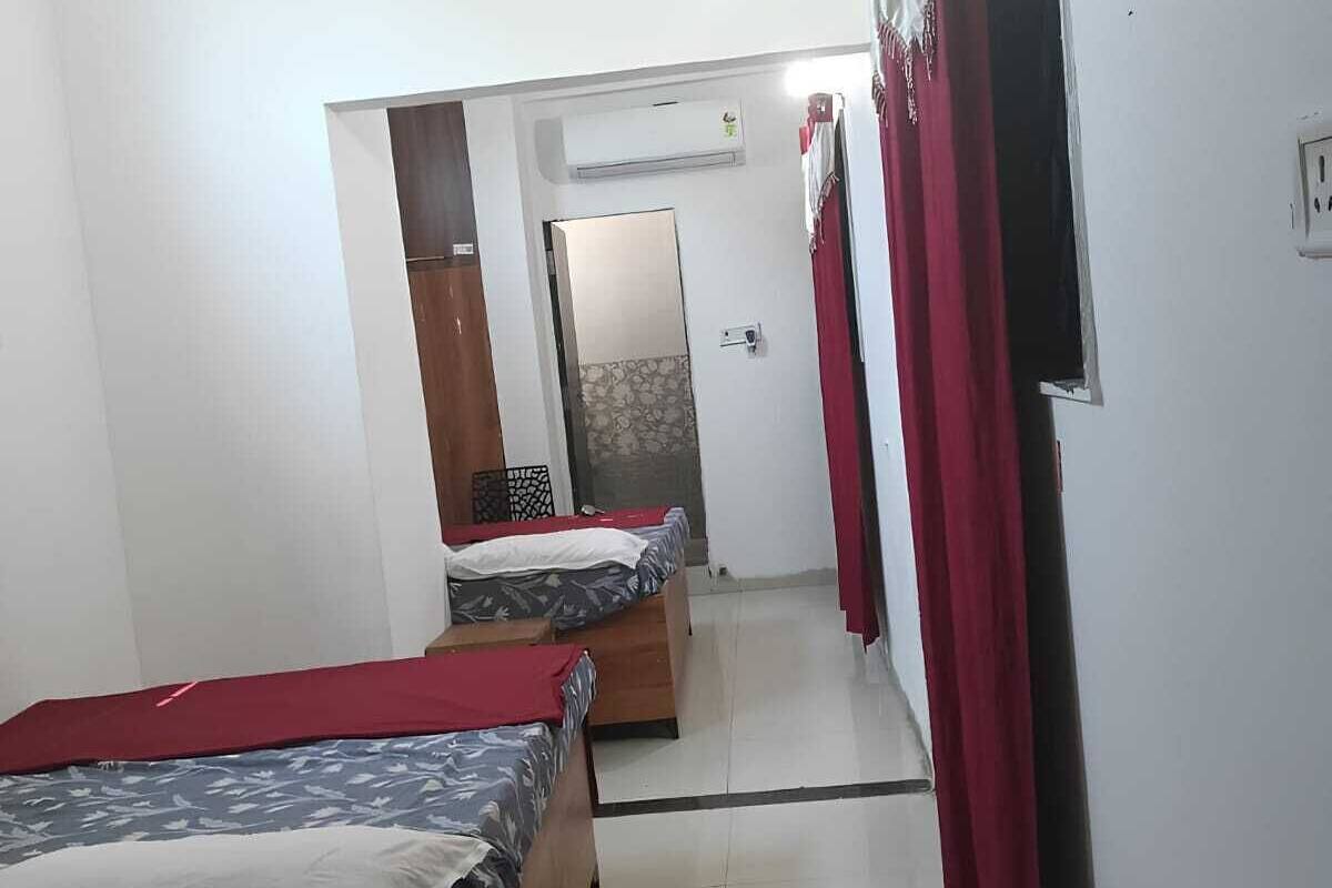 Habitación de hotel con dos camas individuales, un armario, un espejo y una puerta que da a otra habitación.