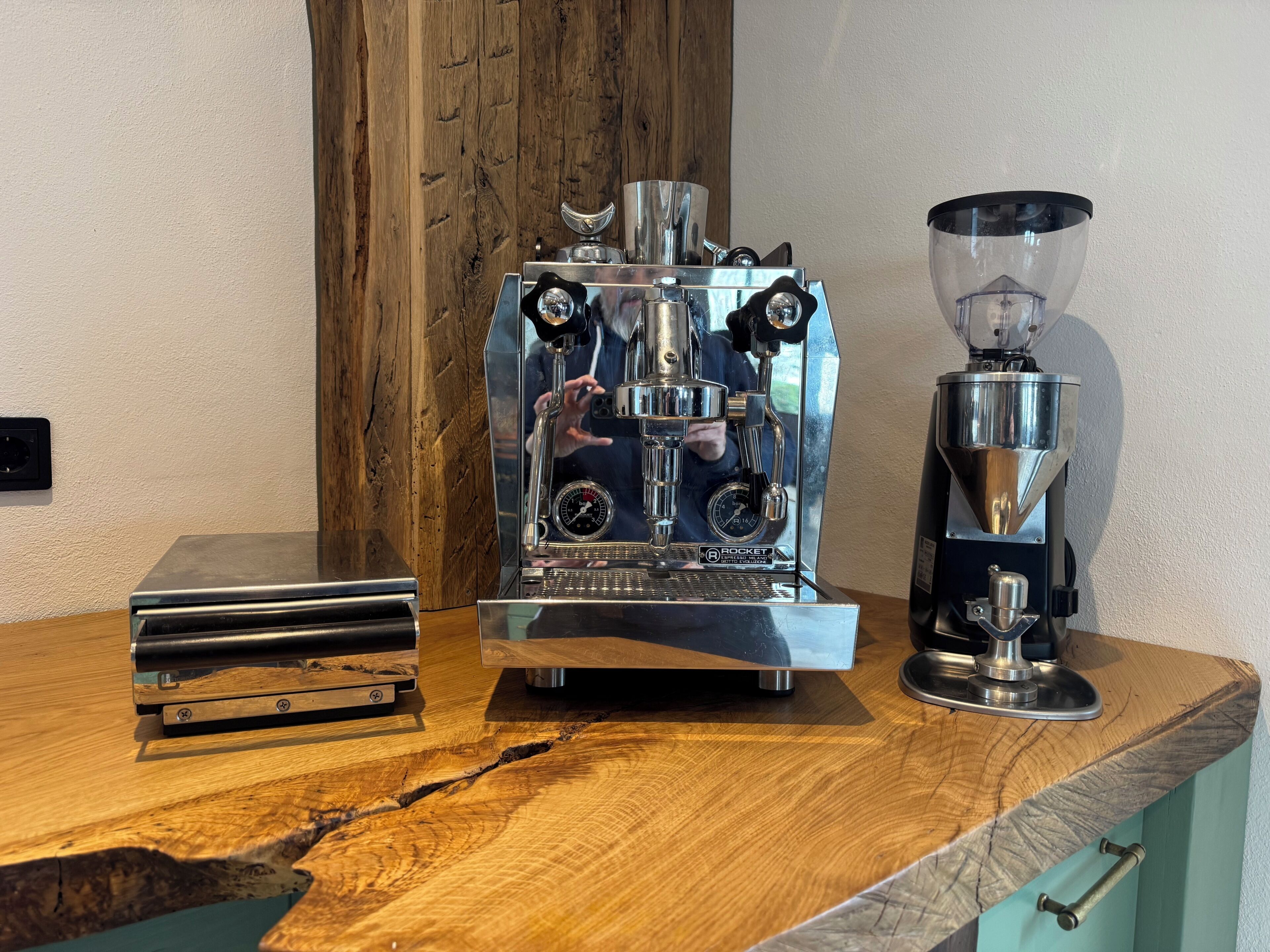 A coffee machine, a grinder, and a stack of books on a wooden table.
