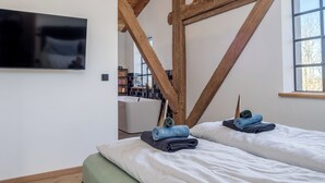 A bedroom with a wooden ceiling, a flat-screen TV mounted on the wall, two beds with neatly folded towels, and a window with a view. - "Barn 1746", luxury apartment for 8 people. Fur noses welcome! (Tating)