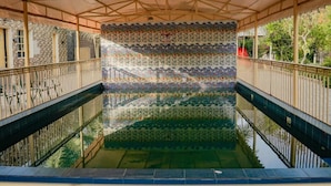 A covered swimming pool with a tiled wall, a metal railing, and a canopy overhead.